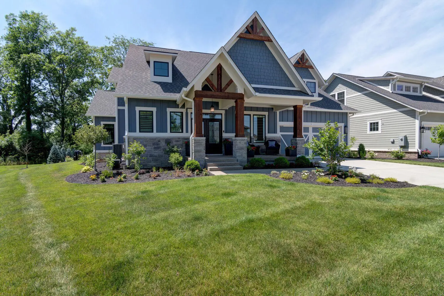 Blue-gray craftsman home with a stone-and-timber gabled entry and a wide lawn