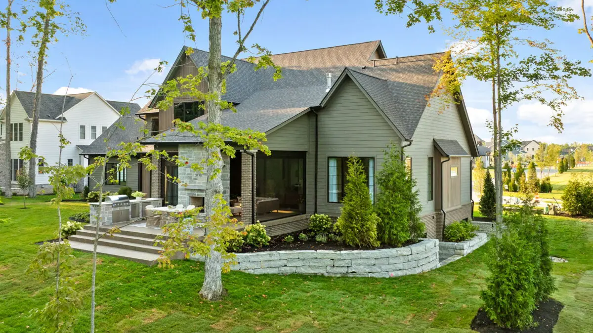 Rear of a gray-green home with a stone-walled patio and a terraced lawn