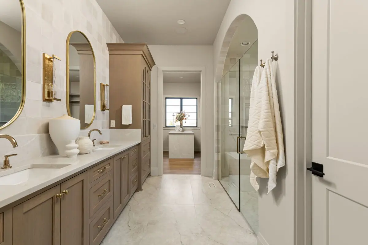 Primary bath with a wood double vanity, arched mirrors, brass sconces and an arched glass shower