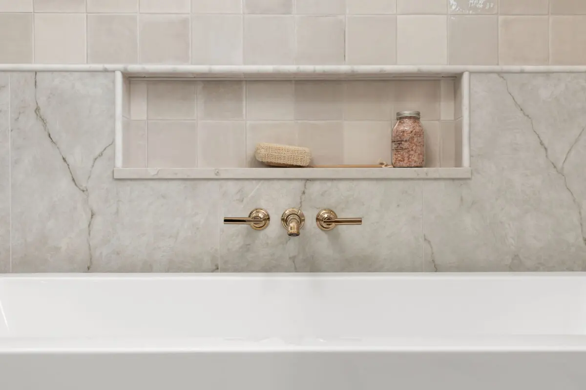 Soaking tub with a marble-look wall, a recessed niche and brass wall-mounted faucet
