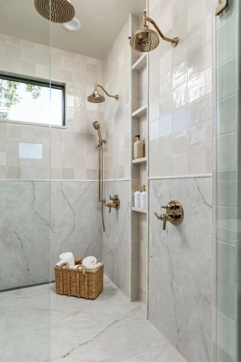 Walk-in shower with stone-look tile, brass fixtures, a built-in niche and a clerestory window