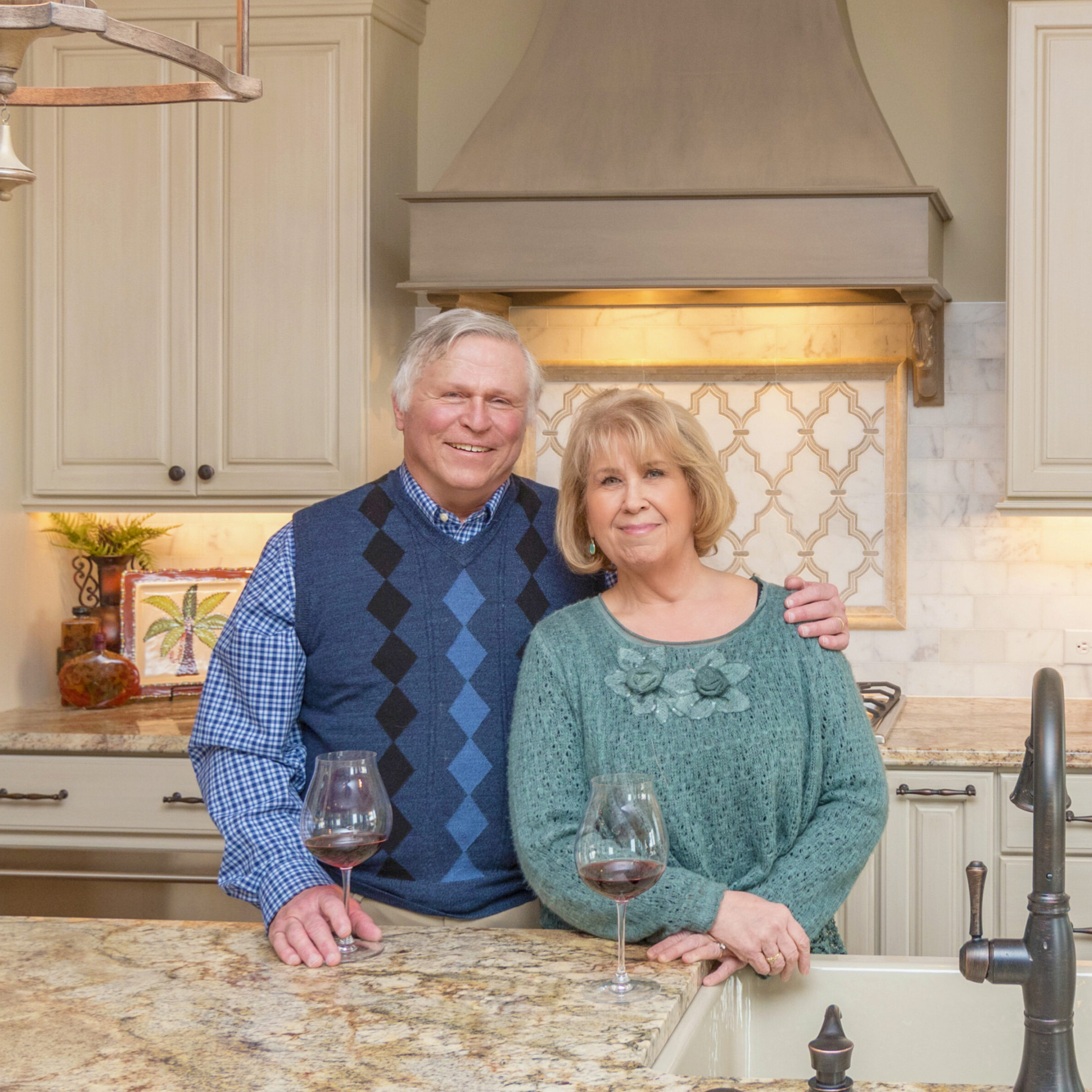 A couple standing in front of a kitchen with wine glasses in their newly built custom home.