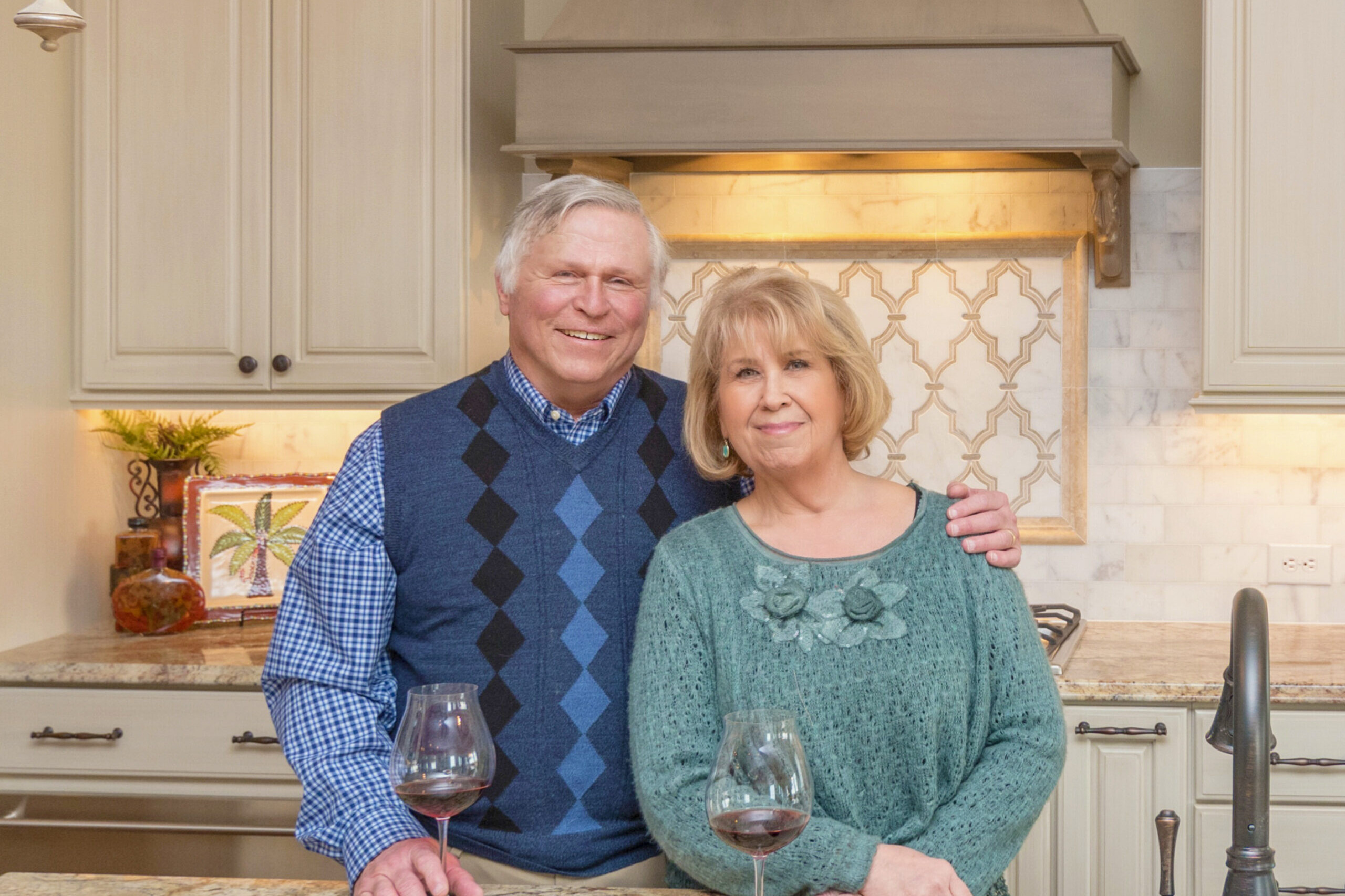 A couple standing in front of a kitchen with wine glasses in their newly built custom home.