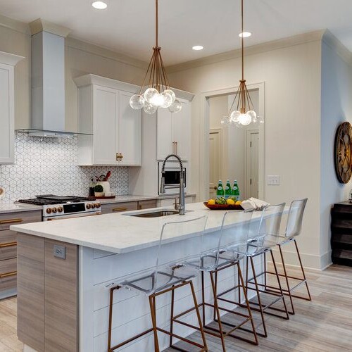 A white kitchen with wood floors and bar stools, located in a new home construction in Indianapolis, Indiana.