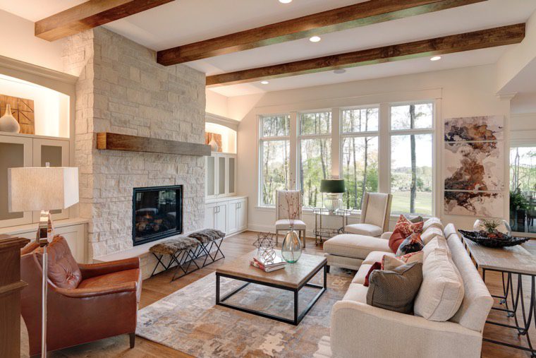 A living room with a stone fireplace and wooden beams in a custom-built home in Carmel, Indiana.
