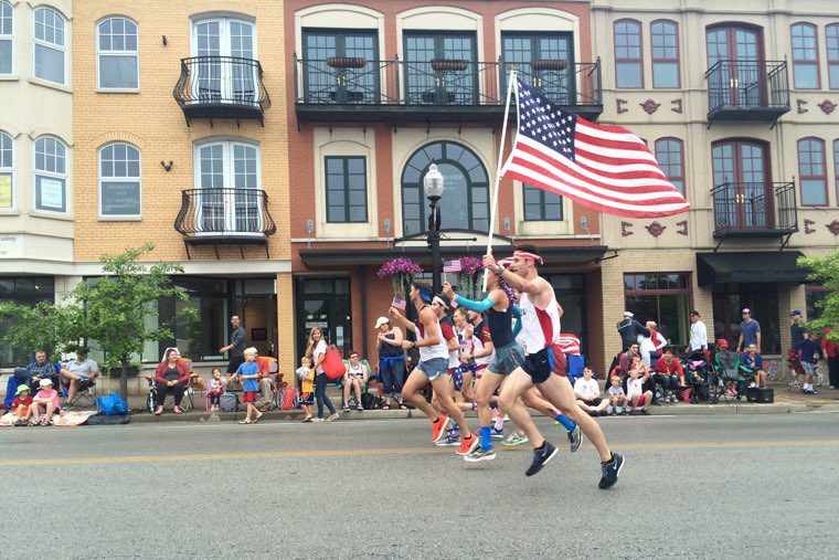 A group of people running down a street with an american flag in Carmel, Indiana.