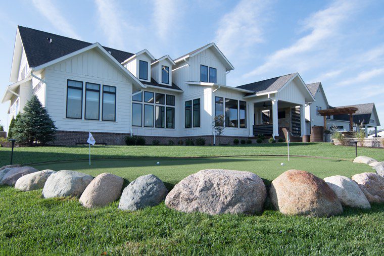 A custom home with a putting green in front of it.