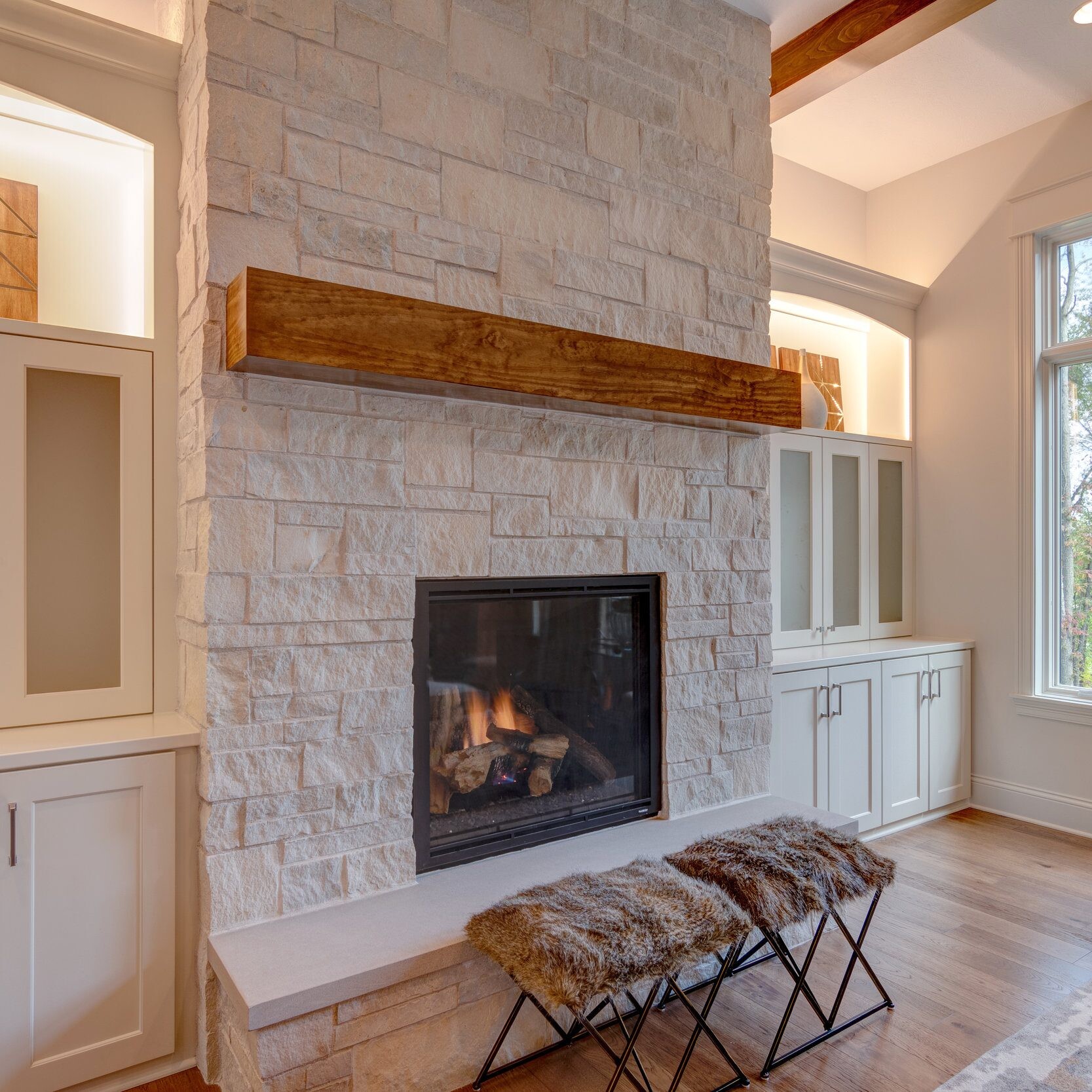 A newly constructed living room with a stone fireplace and white cabinets, built by a custom home builder in Carmel, Indiana.