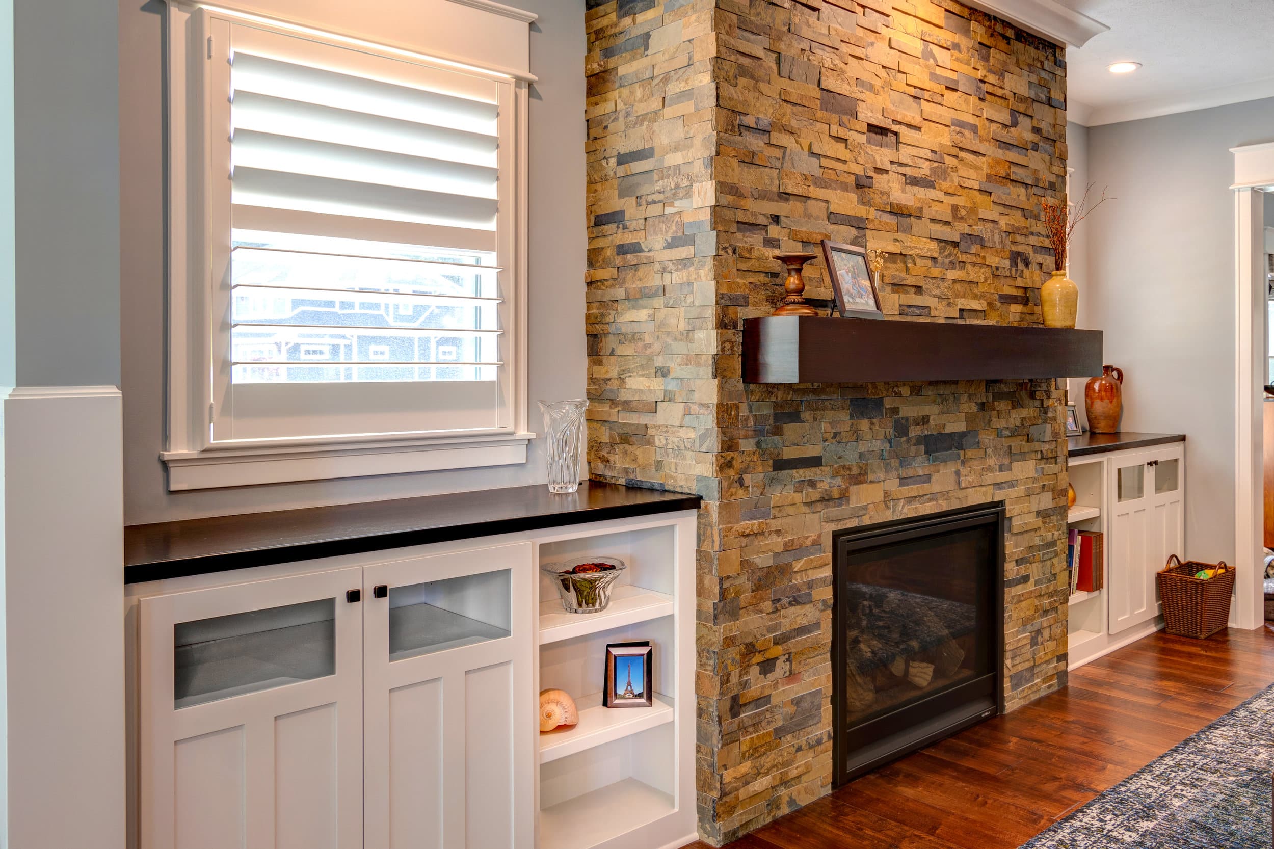 A living room with a stone fireplace and white cabinets in a custom home.