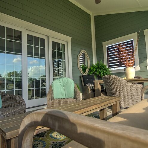 A porch with wicker furniture and a ceiling fan, designed by a luxury custom home builder in Fishers Indiana.