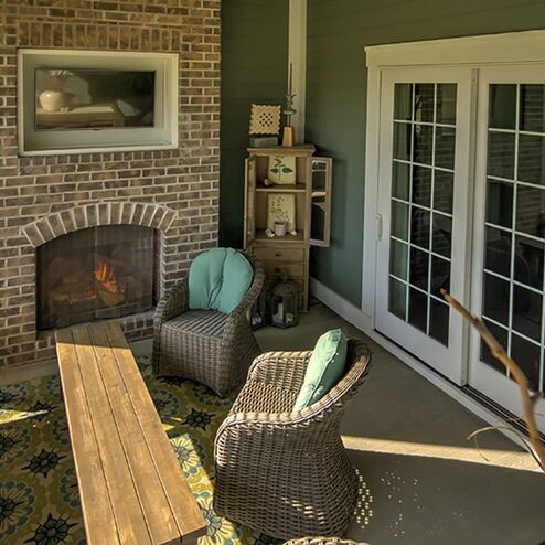 A brick patio with wicker furniture and a fireplace, perfect for enjoying the outdoors in Fishers Indiana custom homes.