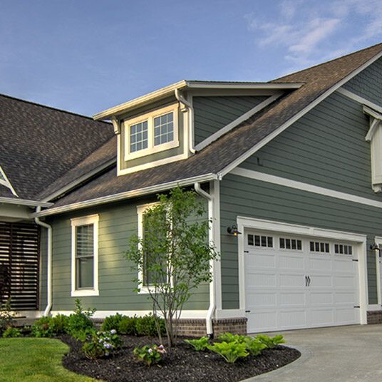 A luxurious custom home with green siding and a garage, built by a leading custom home builder in Carmel Indiana.