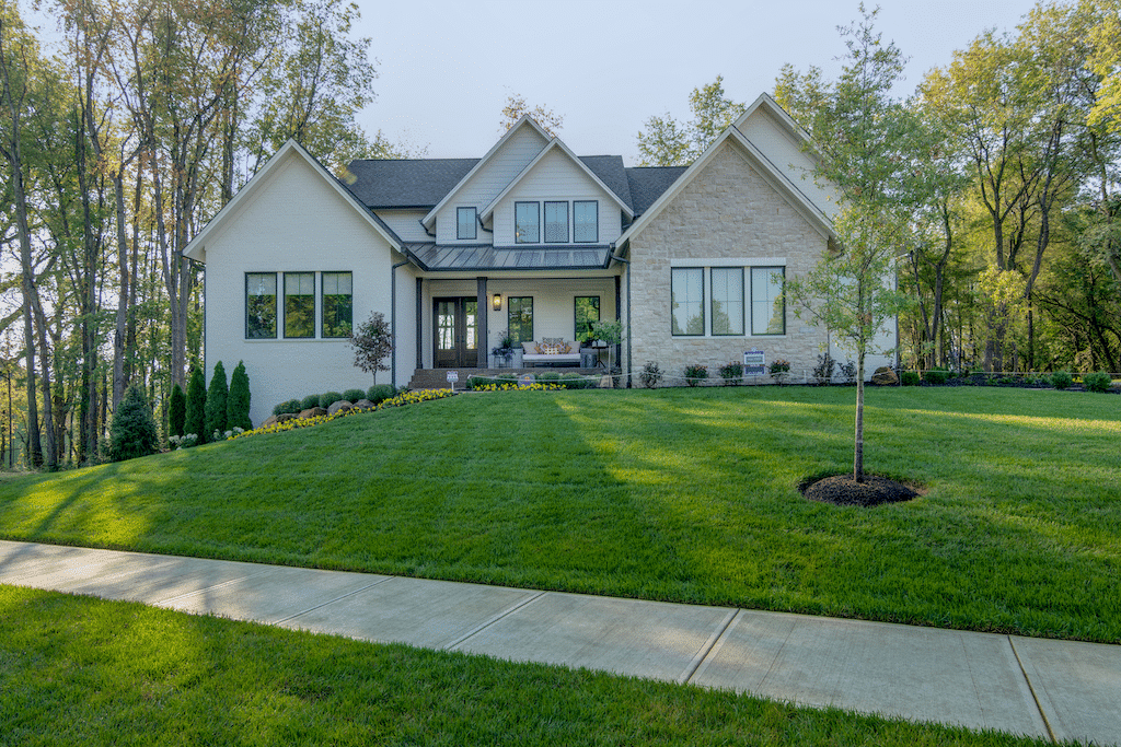 A custom home with a beautifully landscaped front yard, featuring a lush lawn and mature trees.