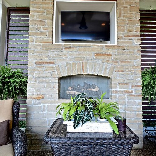 A patio with a stone fireplace, wicker furniture, and a custom home builder in Carmel Indiana.