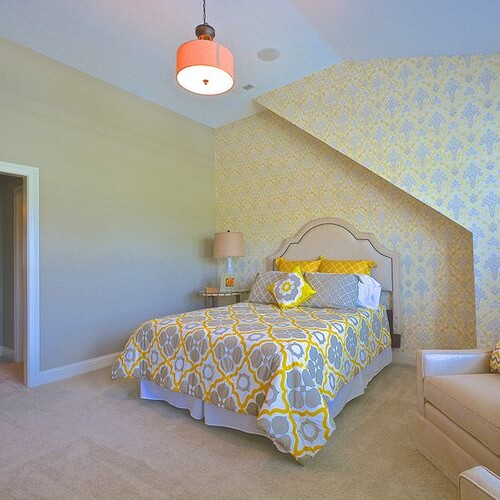 A custom bedroom with a bed and a chair in a yellow and white home.