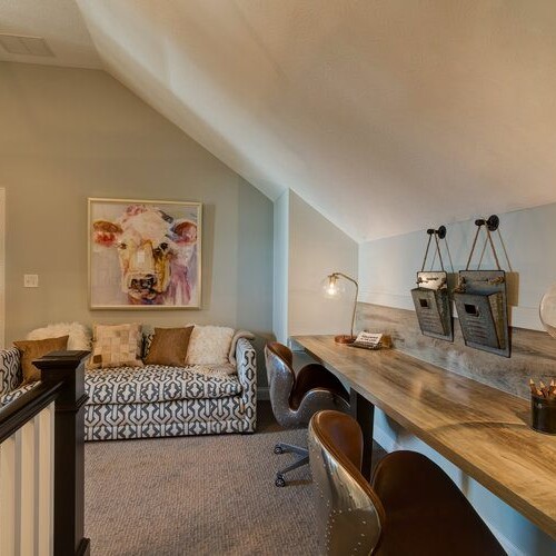 A cozy attic bedroom with a desk and a charming cow painting.