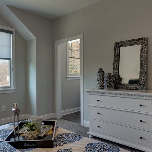 A bedroom with a dresser and a window, located in a custom home for sale in Westfield, Indiana.