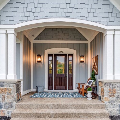 A custom home with a gray front door and stone steps.