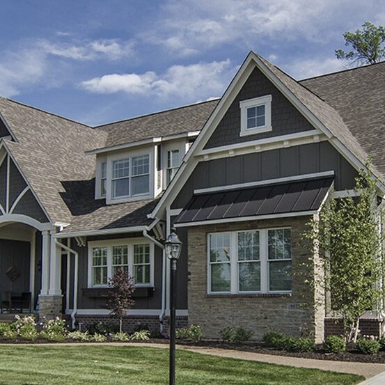 A luxury custom home with gray siding and a large front yard.