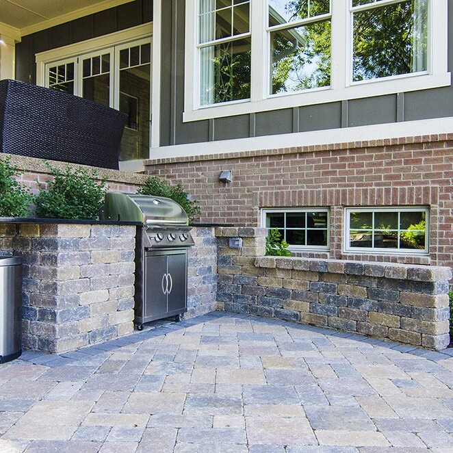 A brick patio with a grill and trash can in a luxury custom home community.