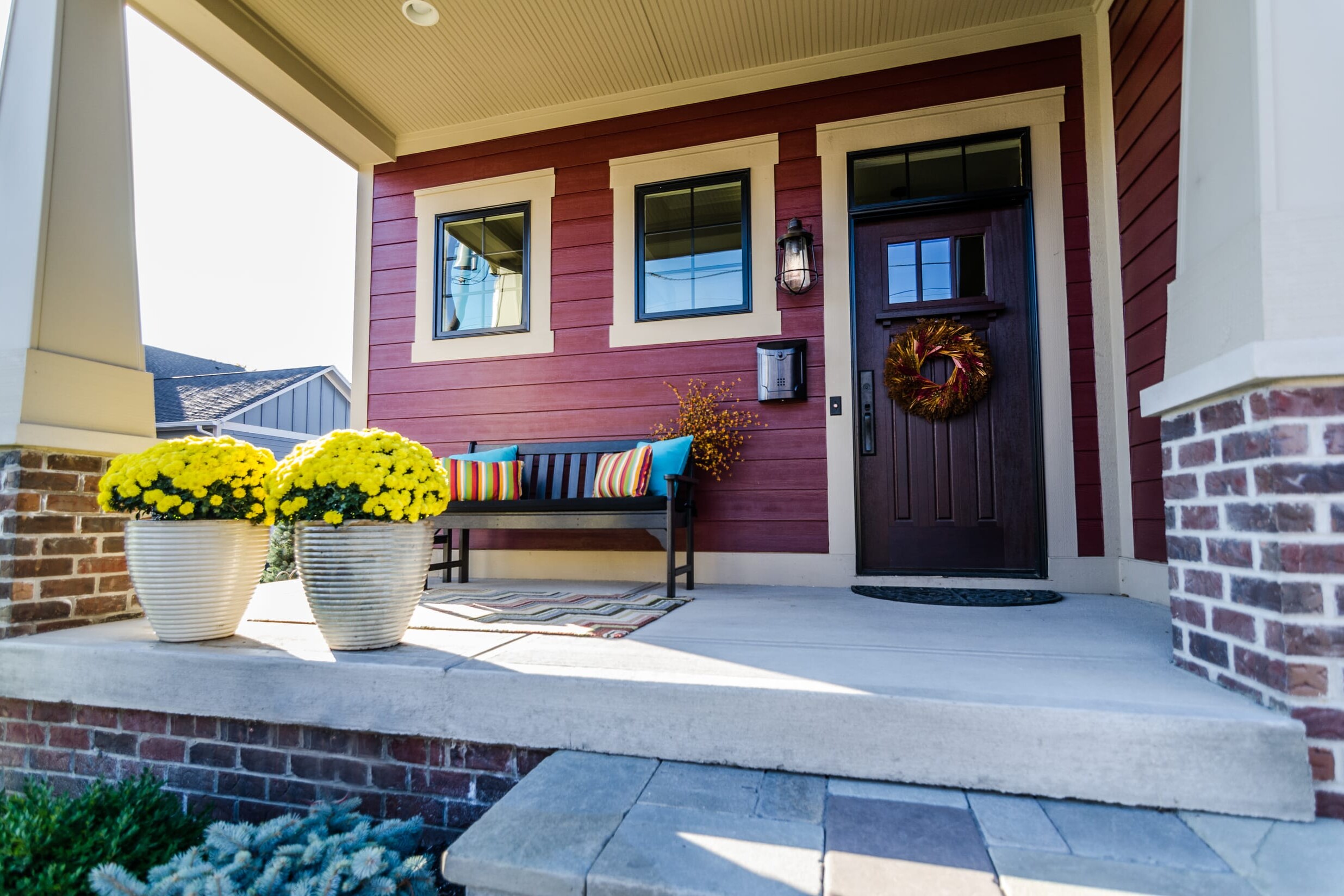 A front porch adorned with potted flowers and a cozy bench, perfect for enjoying the outdoors of your new custom home in Carmel, Indiana.
