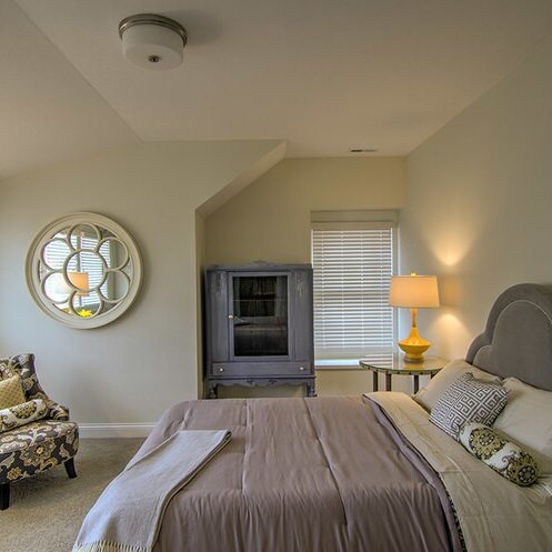 A bedroom with a bed and a chair, designed by a custom home builder in Carmel Indiana.