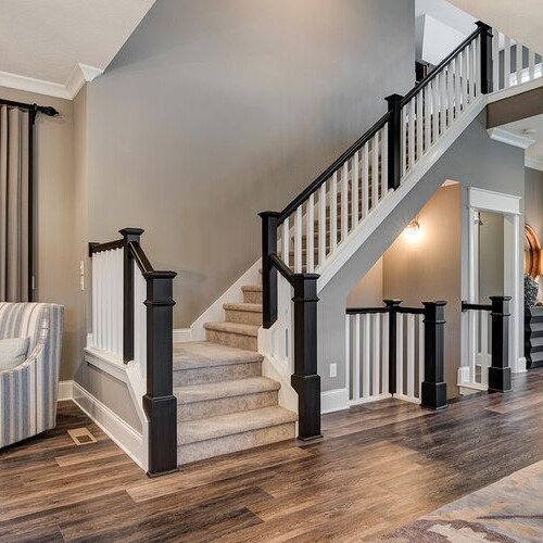 A living room with a staircase and hardwood floors, designed and built by a luxury custom home builder in Westfield, Indiana.