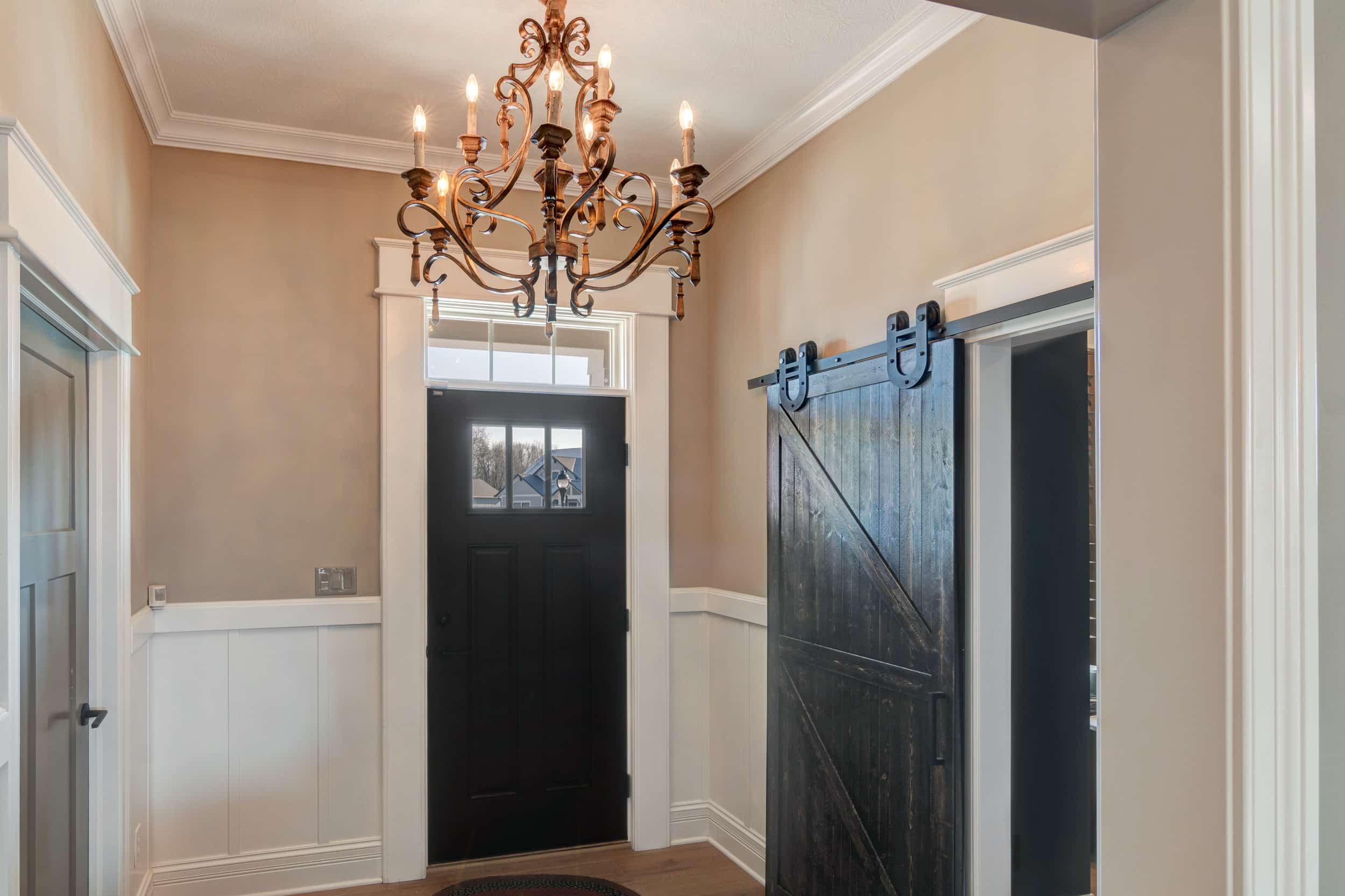 A custom hallway in a new home adorned with a stunning chandelier hanging from the ceiling, leading to an elegant black door.