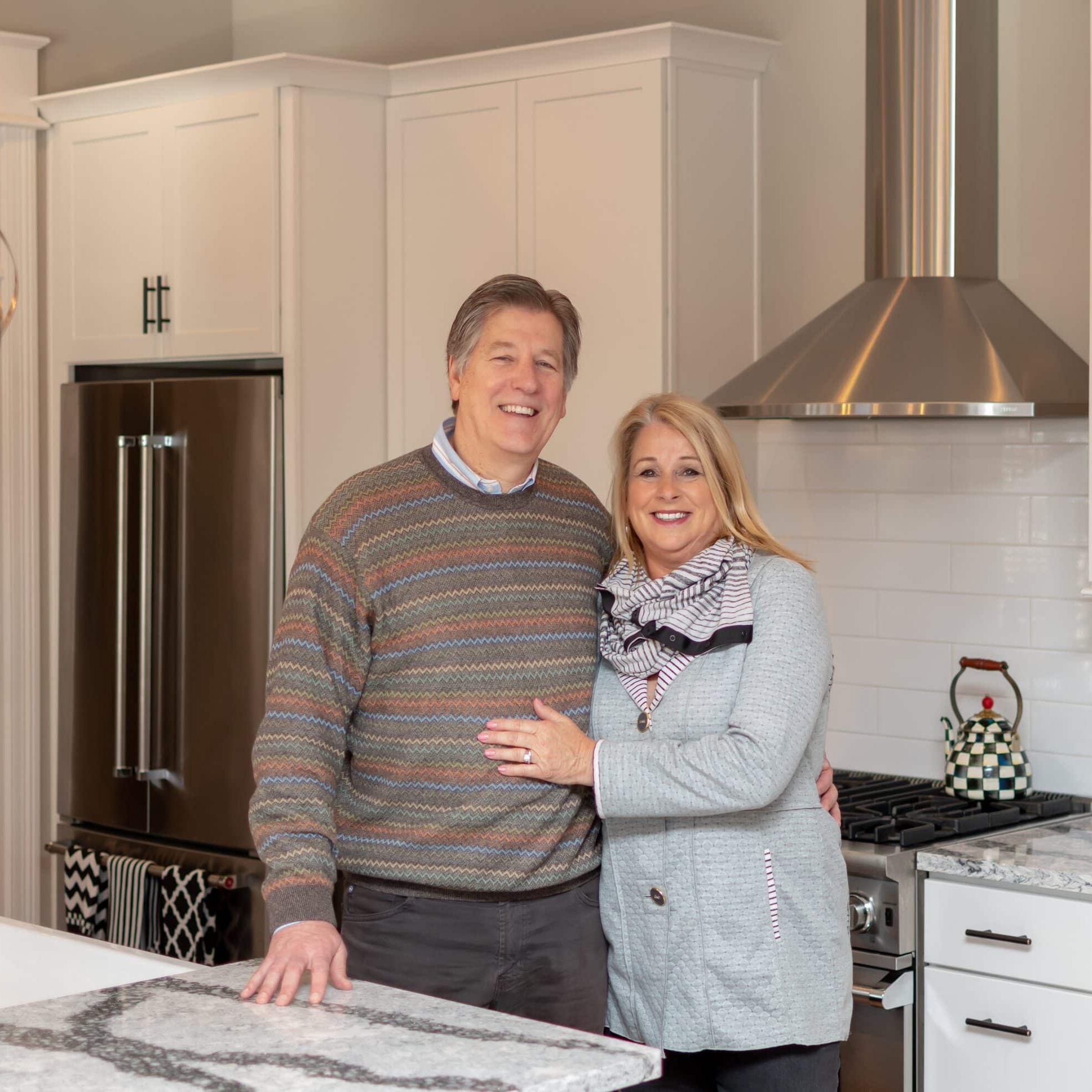 A couple standing in front of a kitchen with marble counter tops in their newly built custom home in Westfield, Indiana.