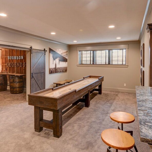 A game room with a shuffleboard table and bar stools, perfect for entertaining in your custom home in Carmel, Indiana.