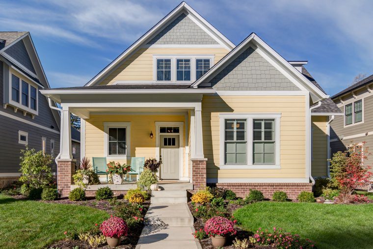 A custom home with a yellow exterior and a front porch for sale in Carmel Indiana.