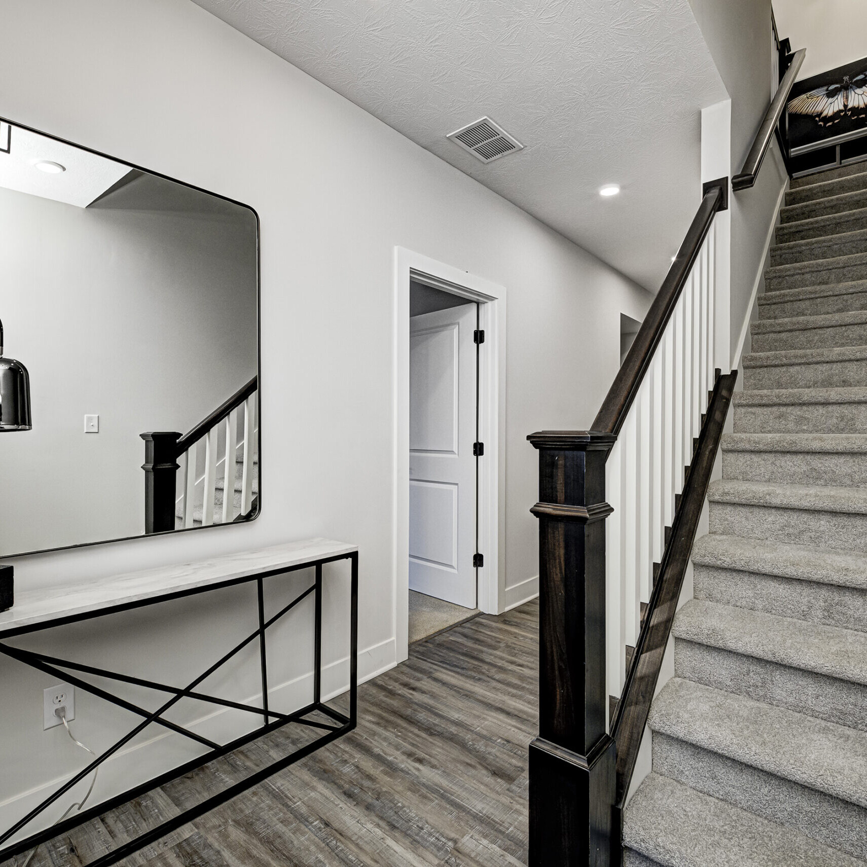 A hallway in a new home with stairs and a mirror.