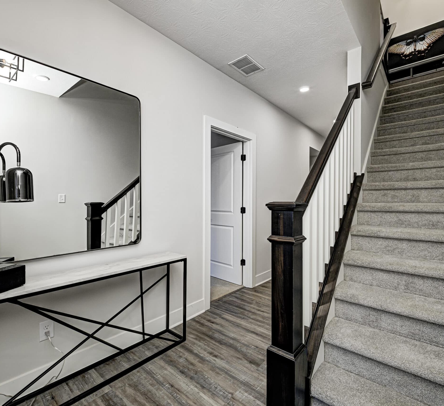 A hallway in a new home with stairs and a mirror.