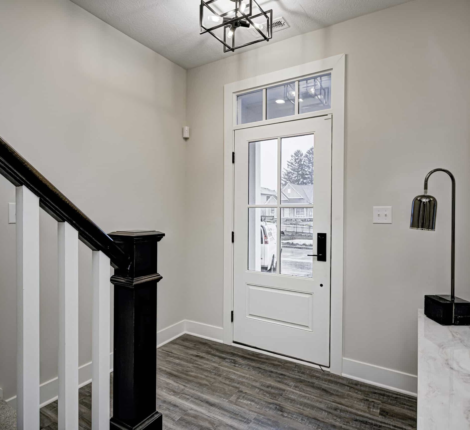 A hallway in a home with a white door and black railing, designed by a custom home builder.