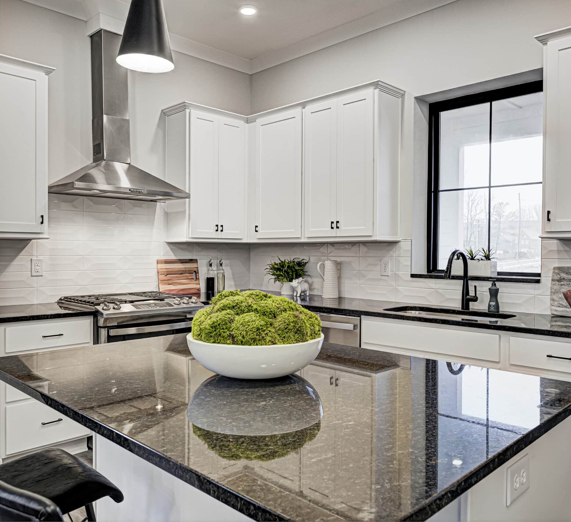 A kitchen with white cabinets and black counter tops, built by a Custom Home Builder Fishers Indiana.