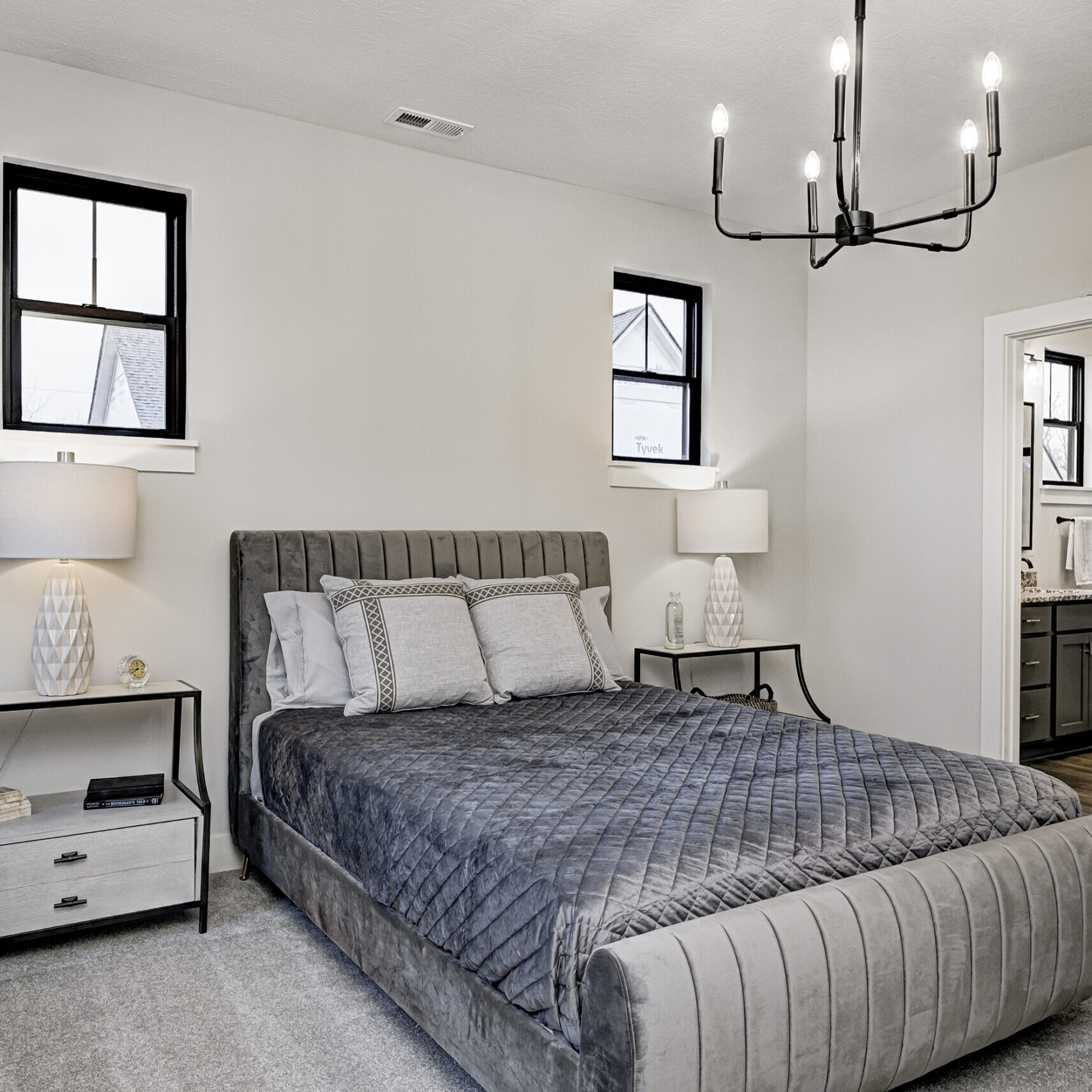 A bedroom with a gray bed and a chandelier in a custom home.