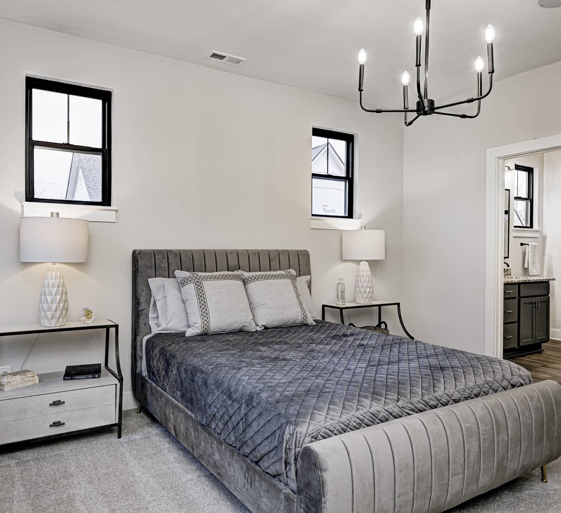 A bedroom with a gray bed and a chandelier in a custom home.
