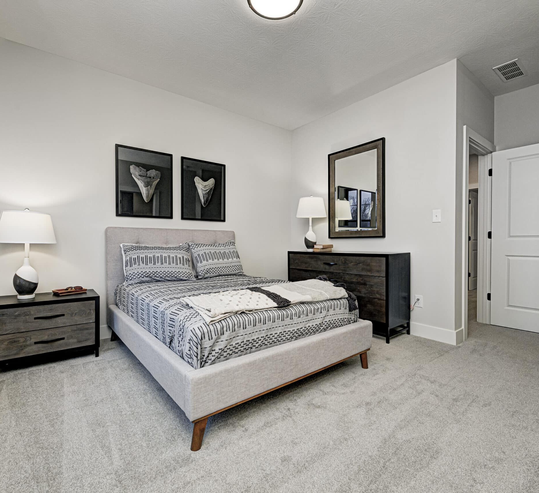 A bedroom with a bed, dresser and mirror in a custom home.