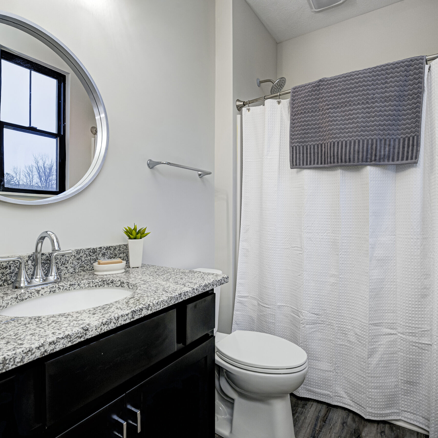 A custom bathroom with a black shower curtain and granite counter top.