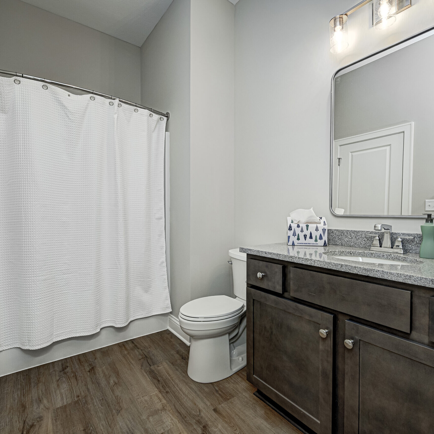 A bathroom with a white shower curtain and wood floors, designed and built by a Custom Home Builder in Carmel Indiana.