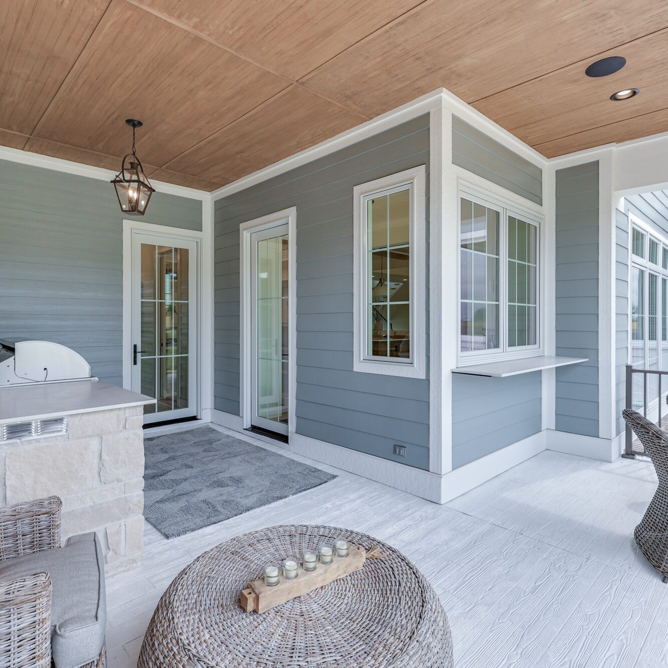 A blue and white porch with wicker furniture and a grill.