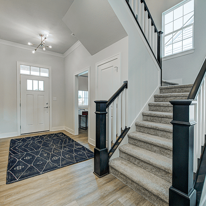 A hallway with a stairway and a black rug.