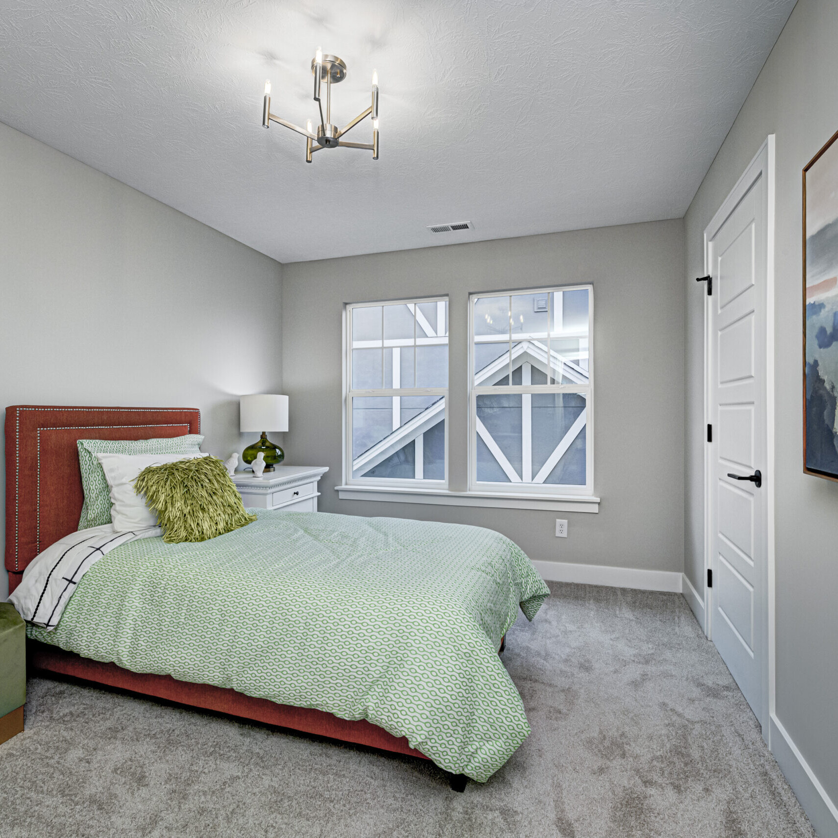 A bedroom with a green bed and a painting on the wall in a custom home.