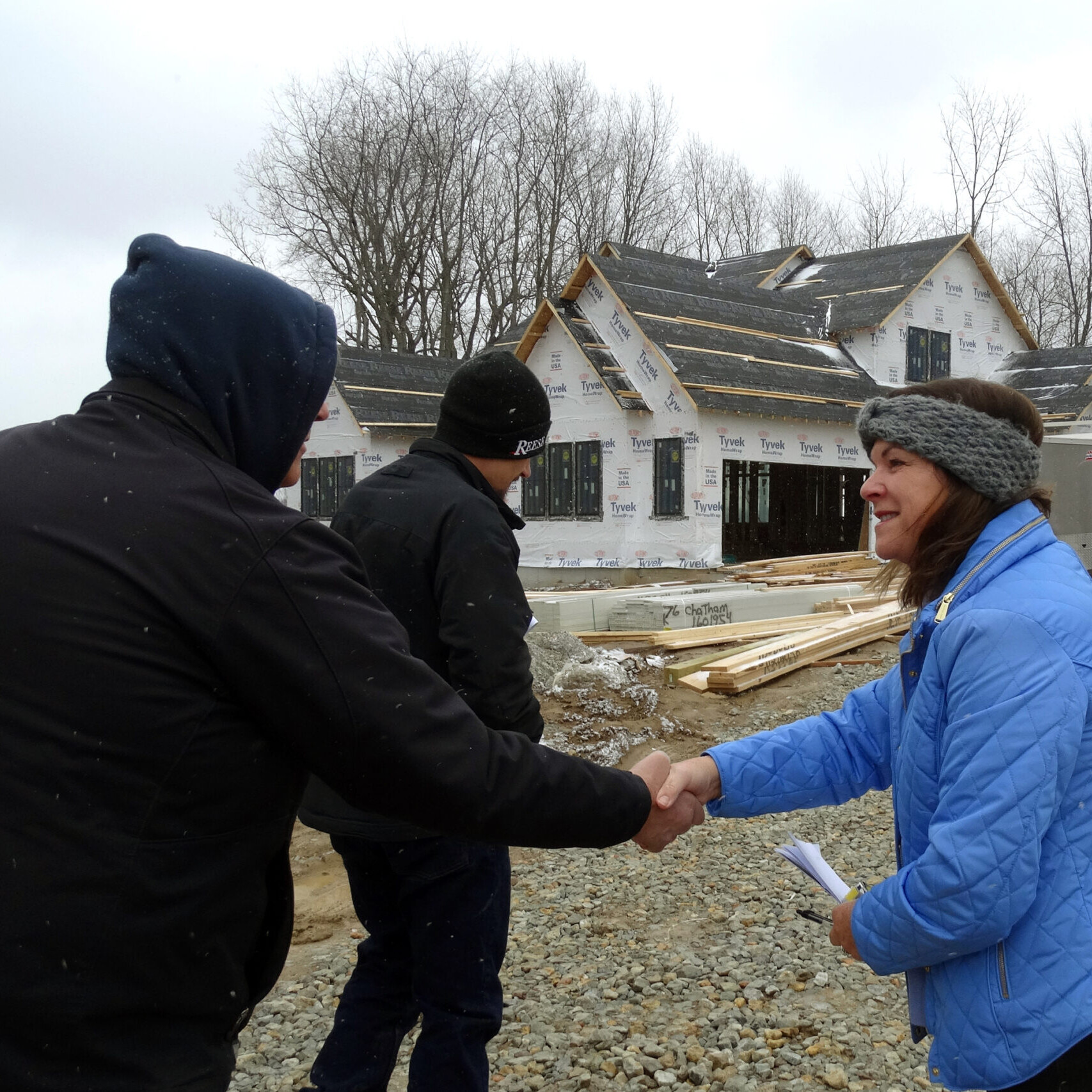 Two people shaking hands in front of a house under construction, symbolizing the partnership between a custom home builder and their clients.