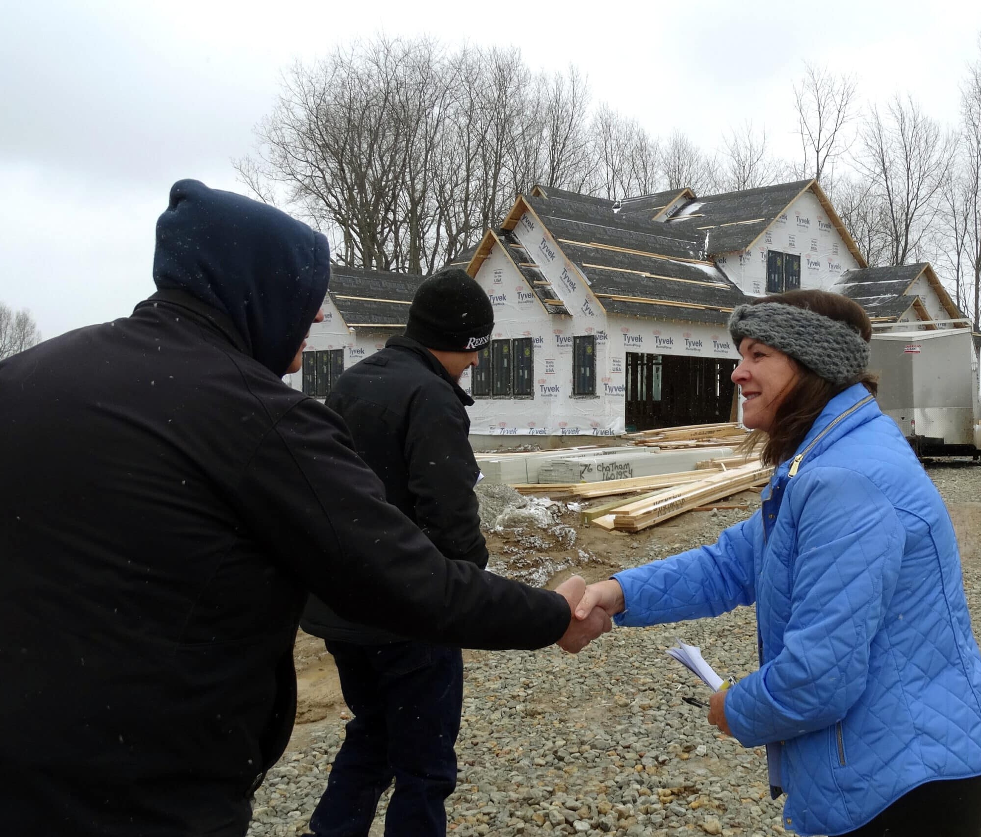 Two people shaking hands in front of a house under construction, symbolizing the partnership between a custom home builder and their clients.