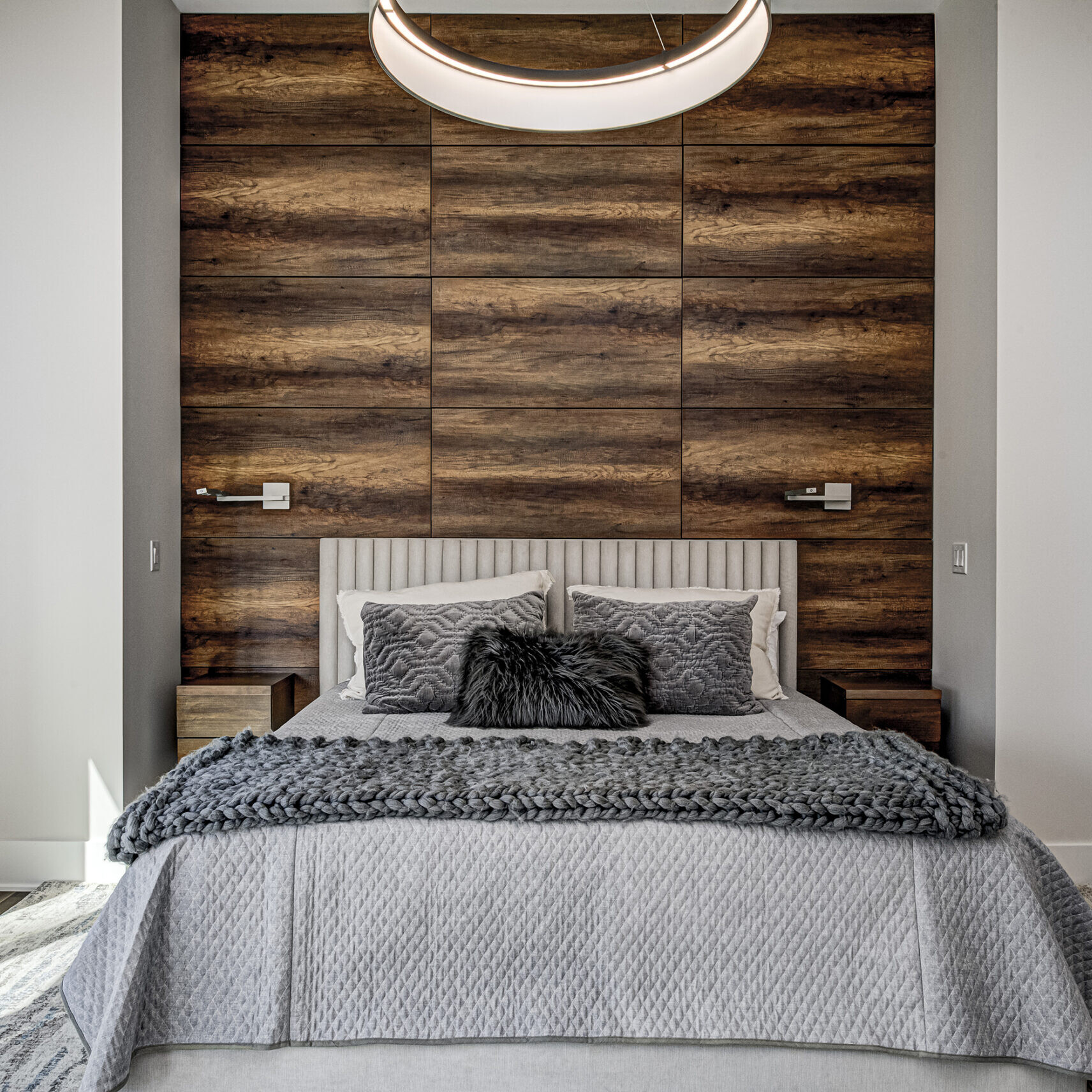 A modern bedroom with wood paneling and a pendant light.