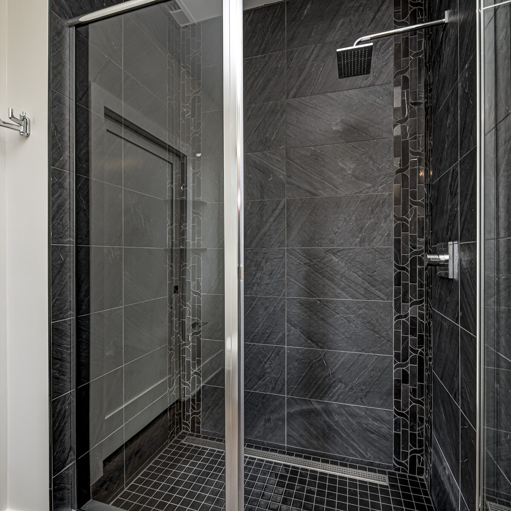 A black tiled shower with a glass door.