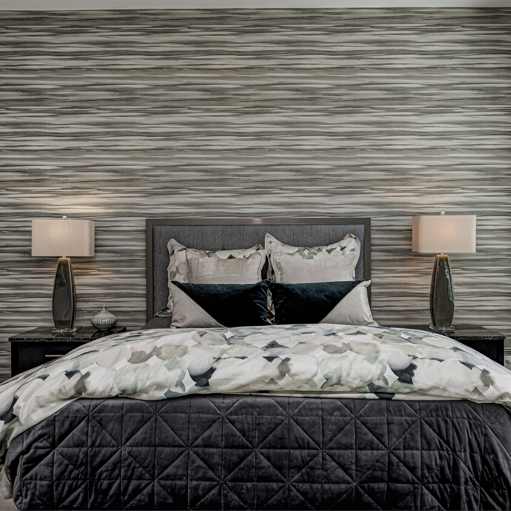 A bed in a bedroom with black and white striped wallpaper.