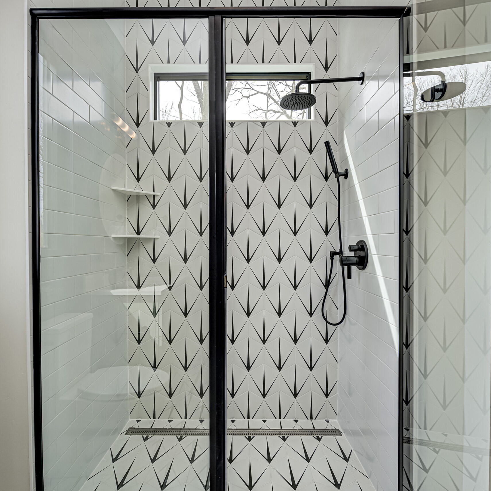 A black and white tiled shower with a glass door.