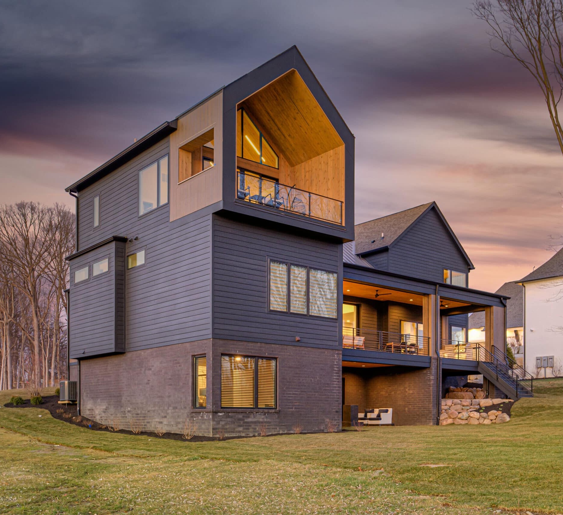 A black house with a deck and a grassy yard.